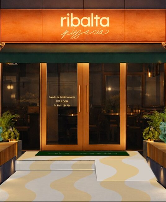 Fachada da Ribalta Pizzaria com letreiro terracota iluminado, porta de vidro e piso em ondas, projeto de ambientação da Unpack Design